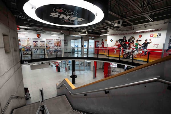 Indoor view of a modern sports facility with stairs, a walkway, and colorful wall advertisements for a sports school.