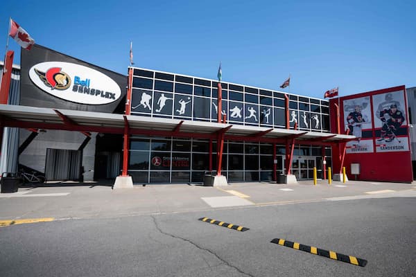 Exterior view of the Bell Sensplex sports facility with silhouettes of athletes on windows and flags on the roof.