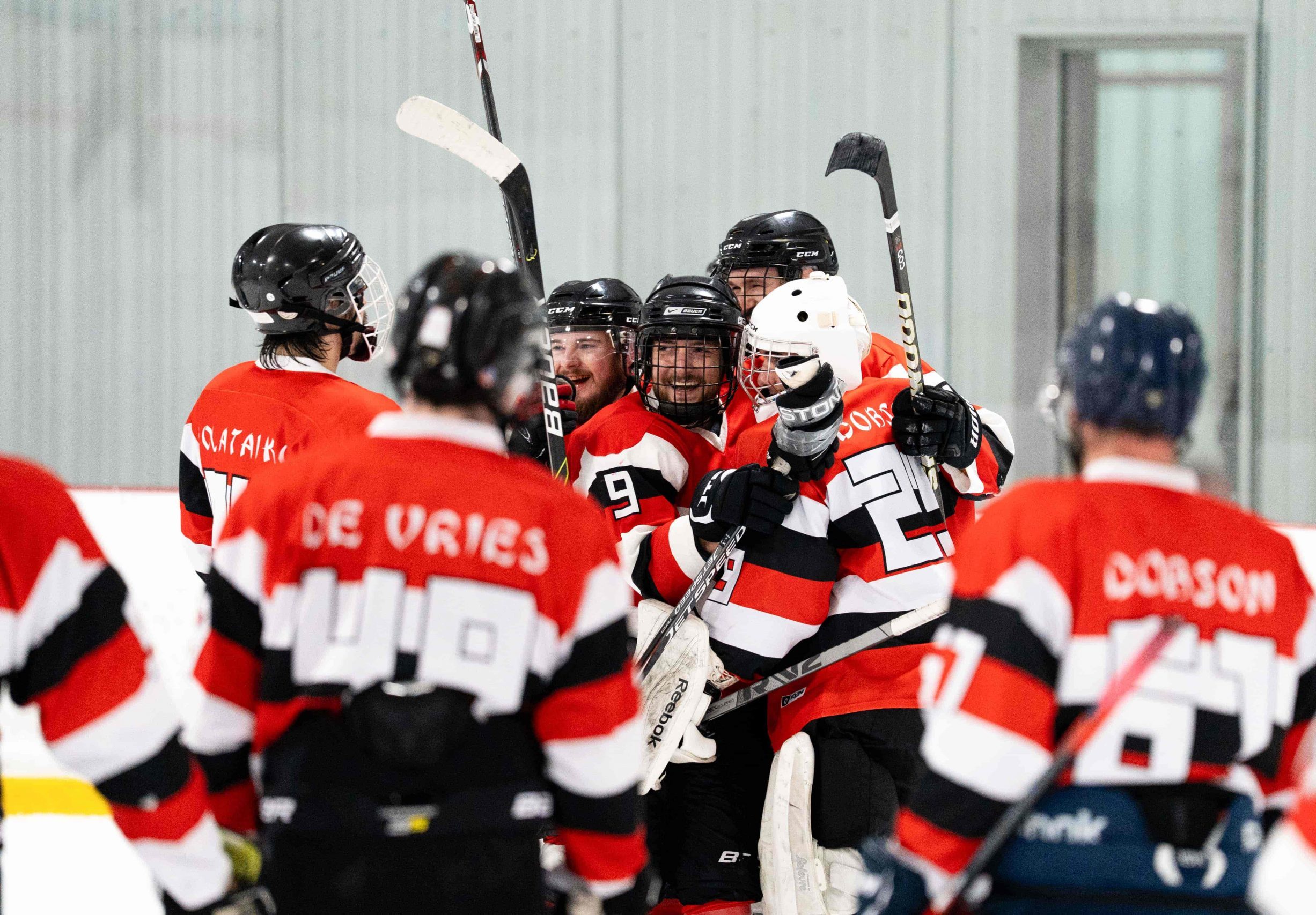 Hockey players in red and black jerseys celebrate together on the ice rink after a game.
