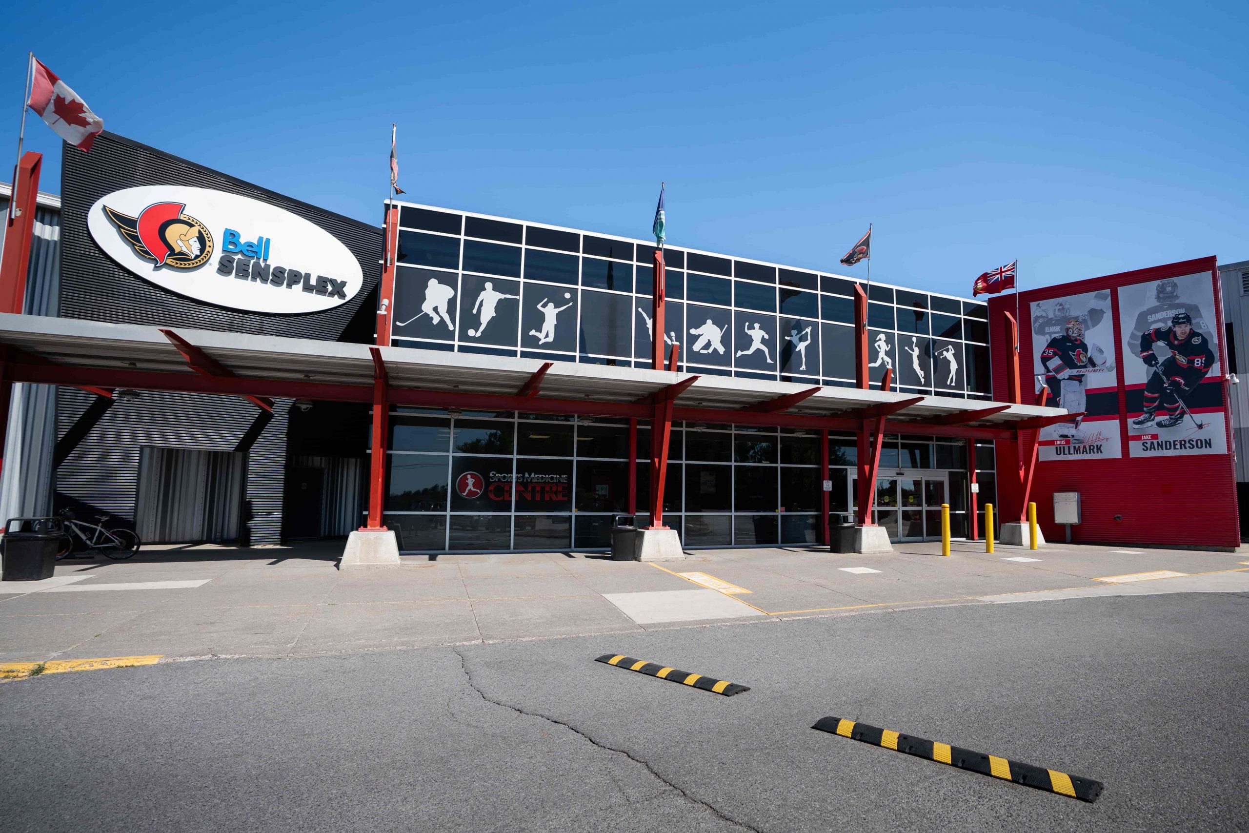 Exterior view of Bell Sensplex sports complex with hockey-themed graphics and player murals on a sunny day.