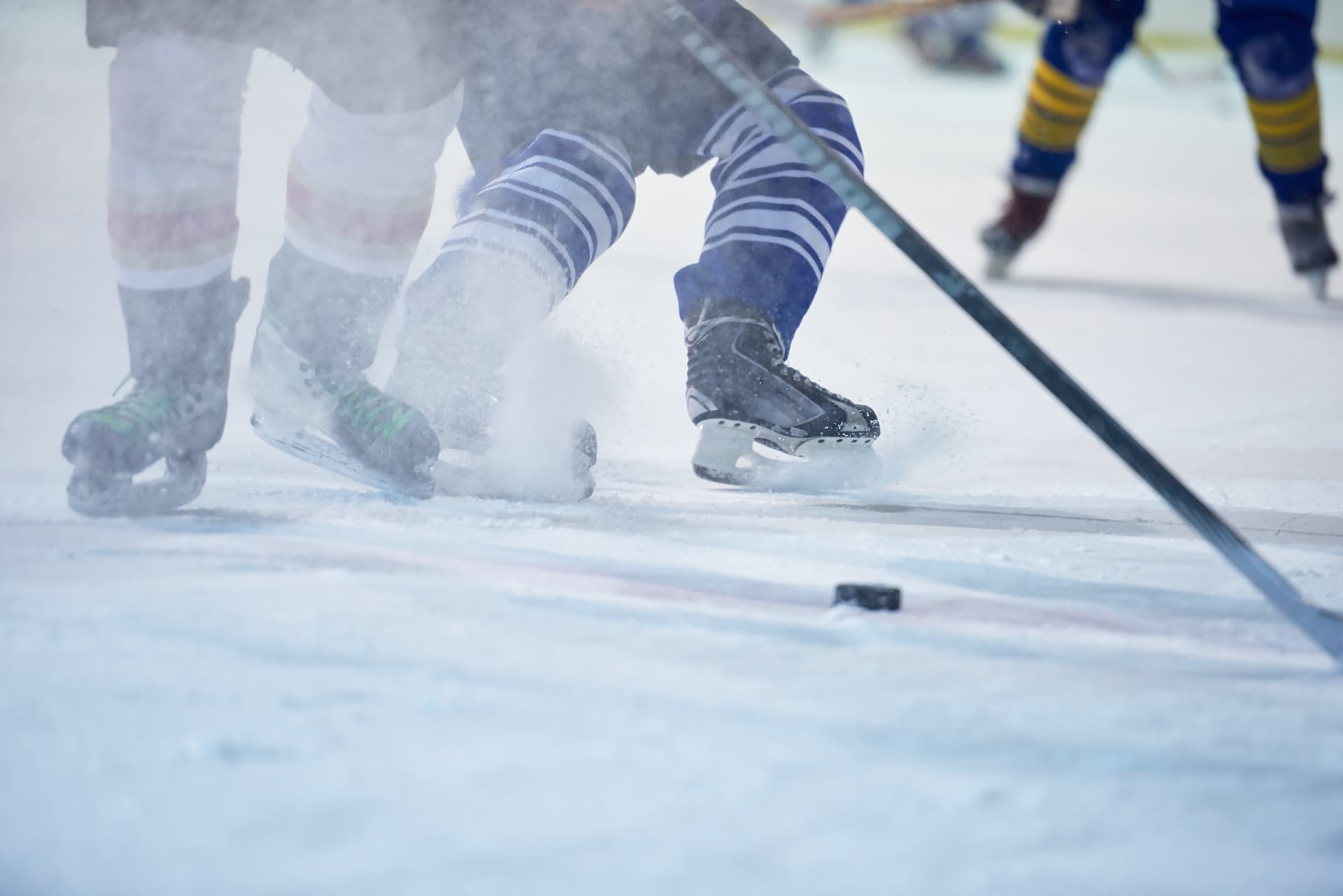 Close-up of hockey players' legs on ice, battling for the puck during a game, with skates and sticks in motion.