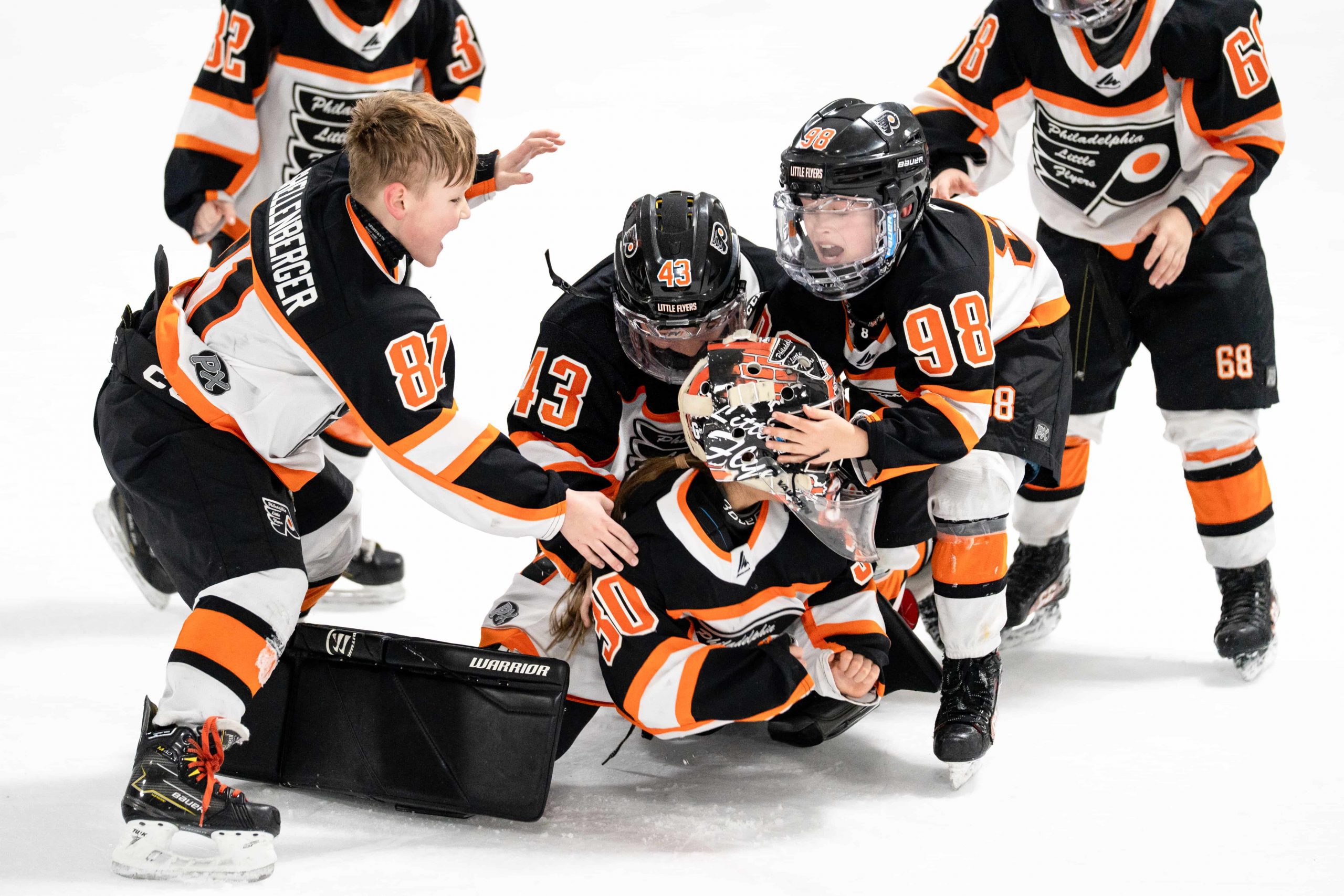Des jeunes joueurs de hockey vêtus d'uniformes noirs et orange font la fête ensemble sur la glace après un match.