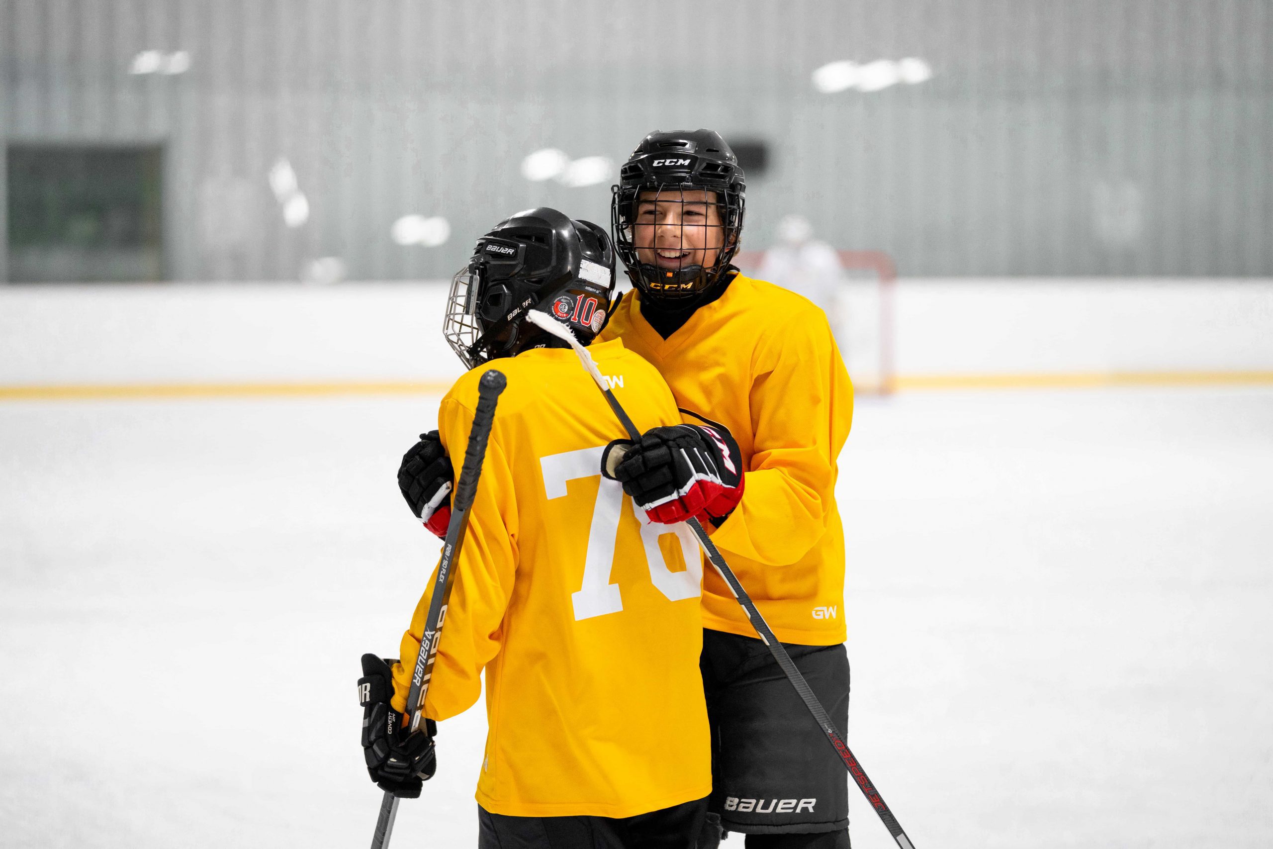 Two hockey players in yellow jerseys and helmets stand on the ice, one with an arm around the other.