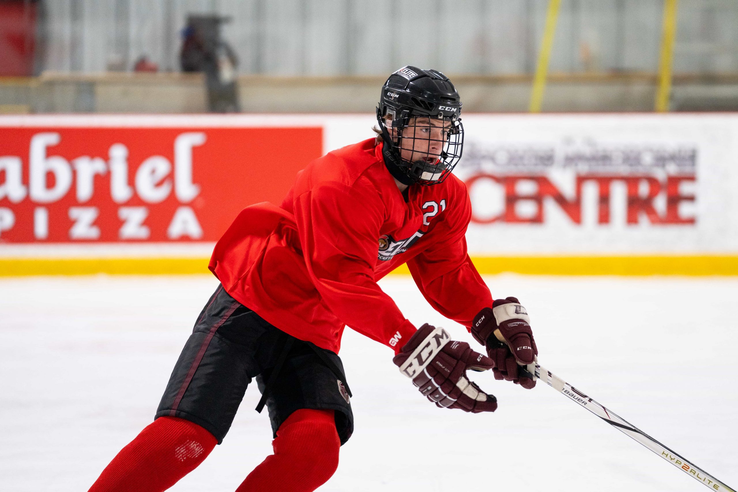Hockey player in red jersey and black helmet skating on ice during a game or practice.