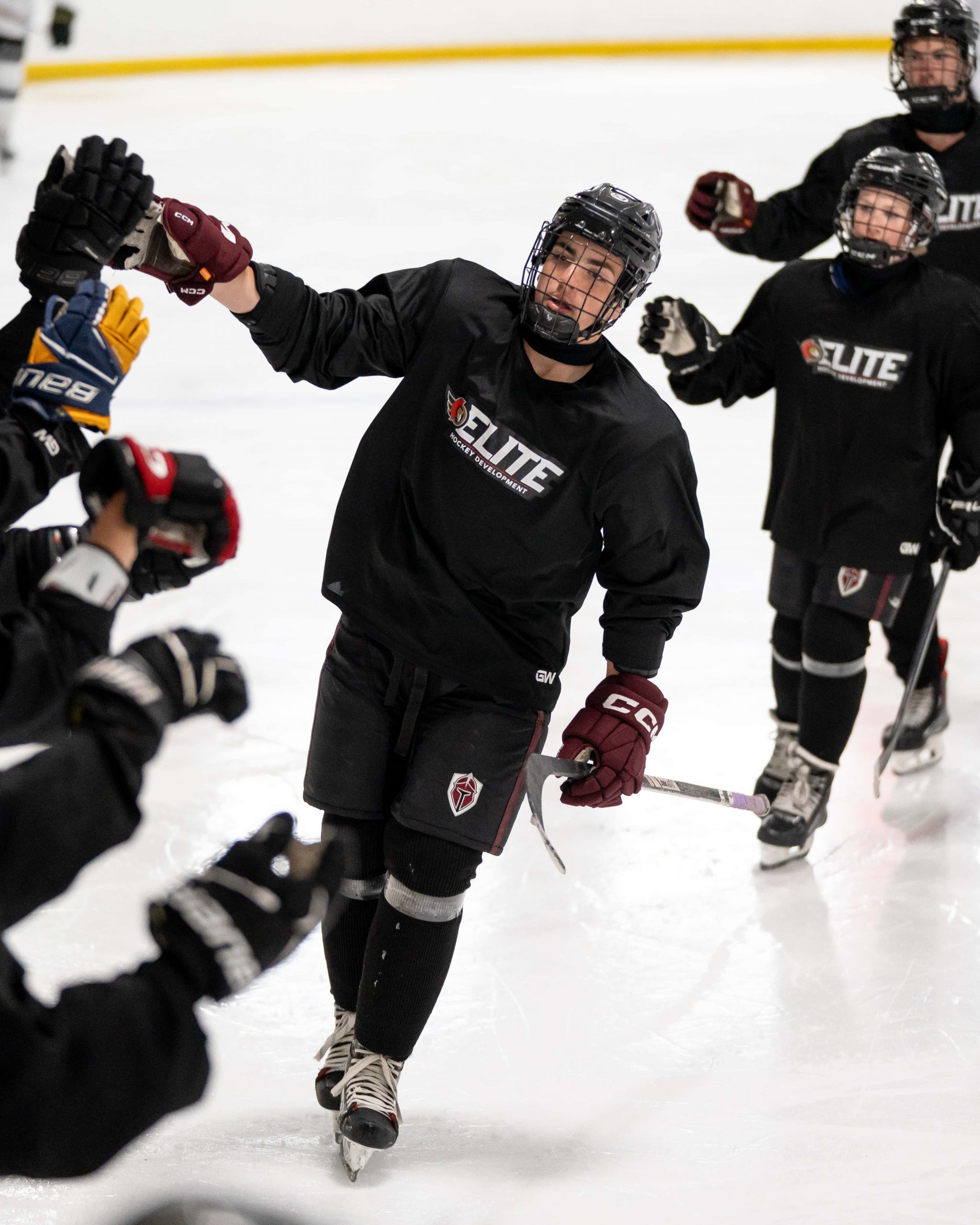 A hockey player in black uniform gives high-fives to teammates while skating on the ice rink.