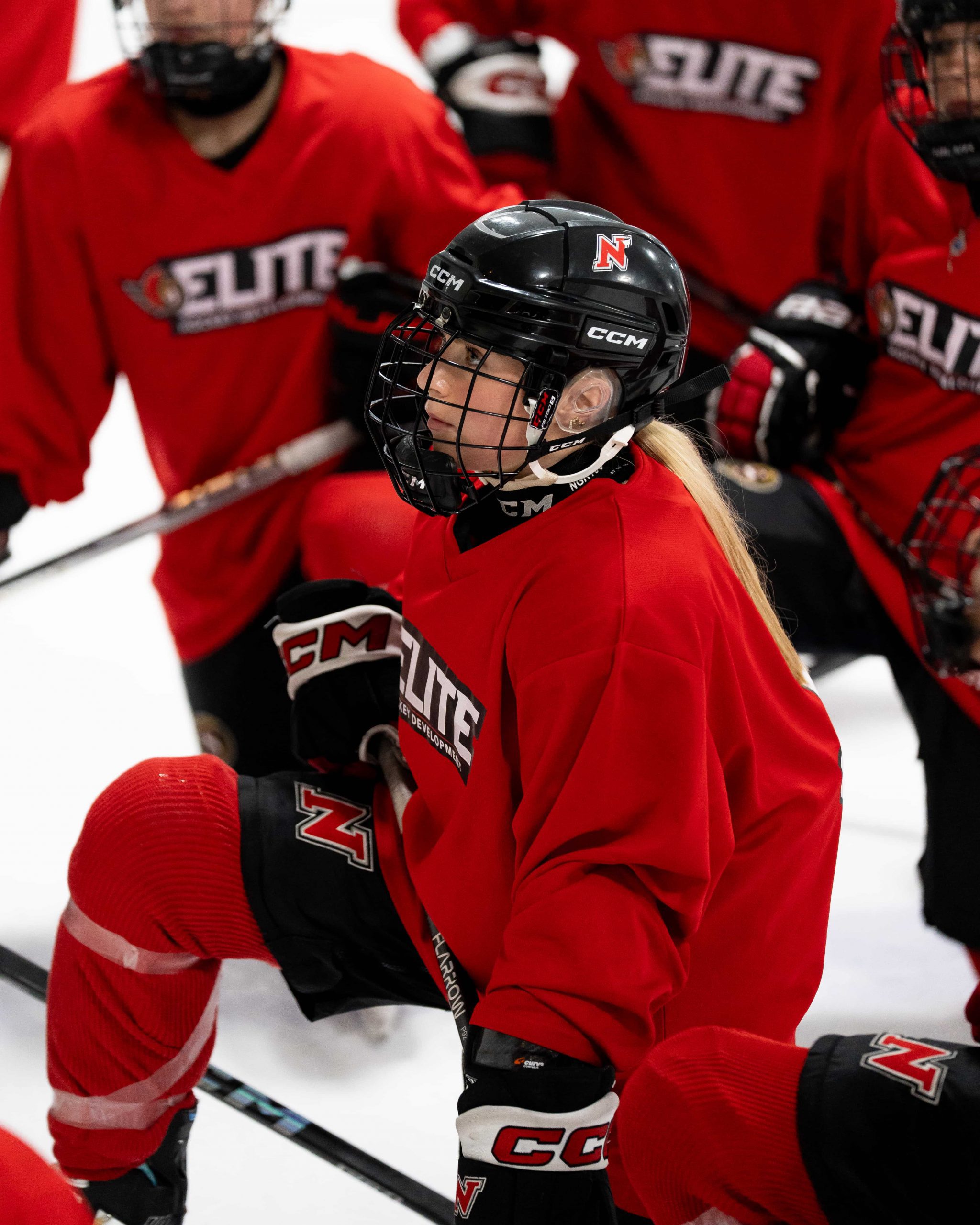 A hockey player in red gear kneels on the ice among teammates during a practice or game.