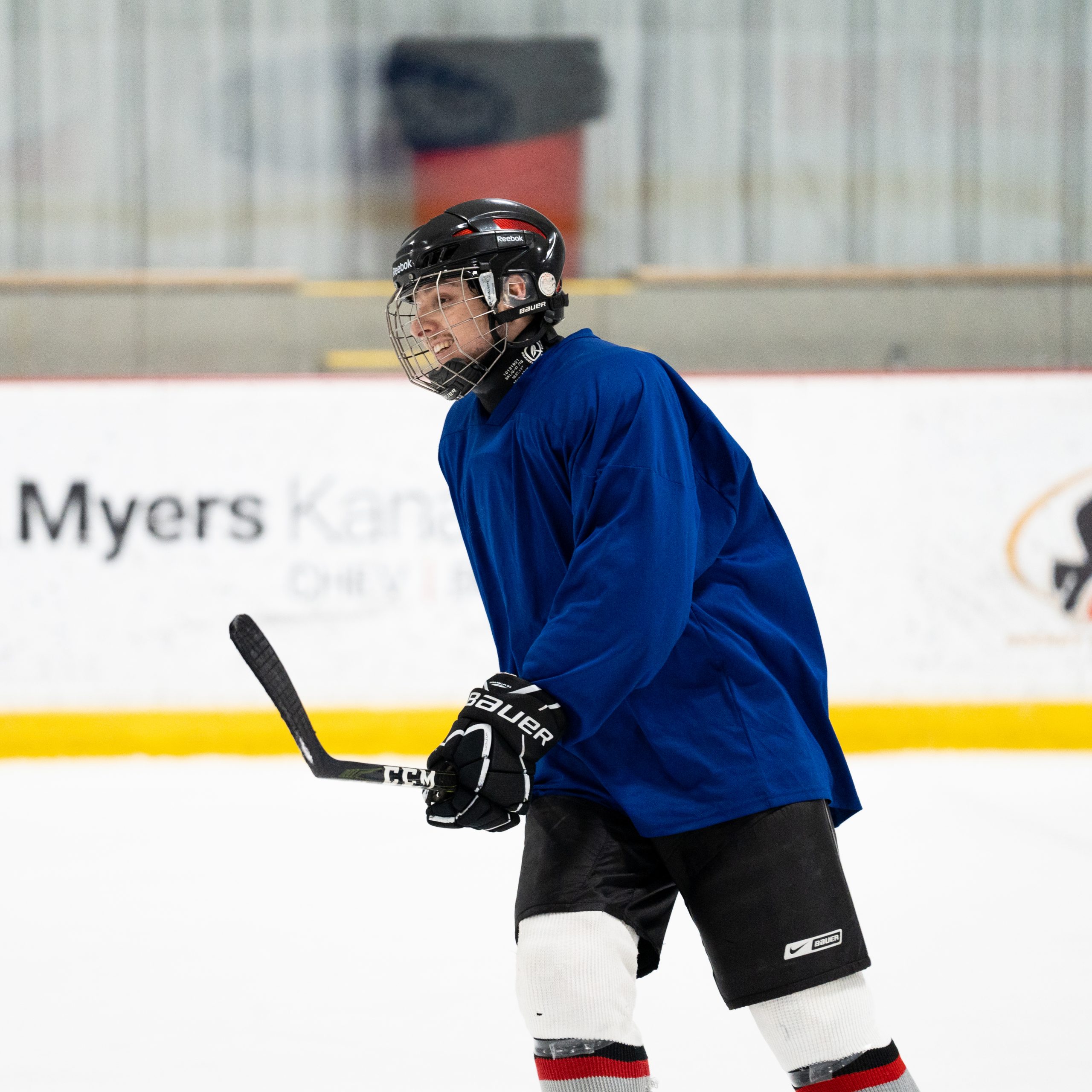 A hockey player in a blue jersey and black helmet stands on the ice holding a hockey stick during practice.