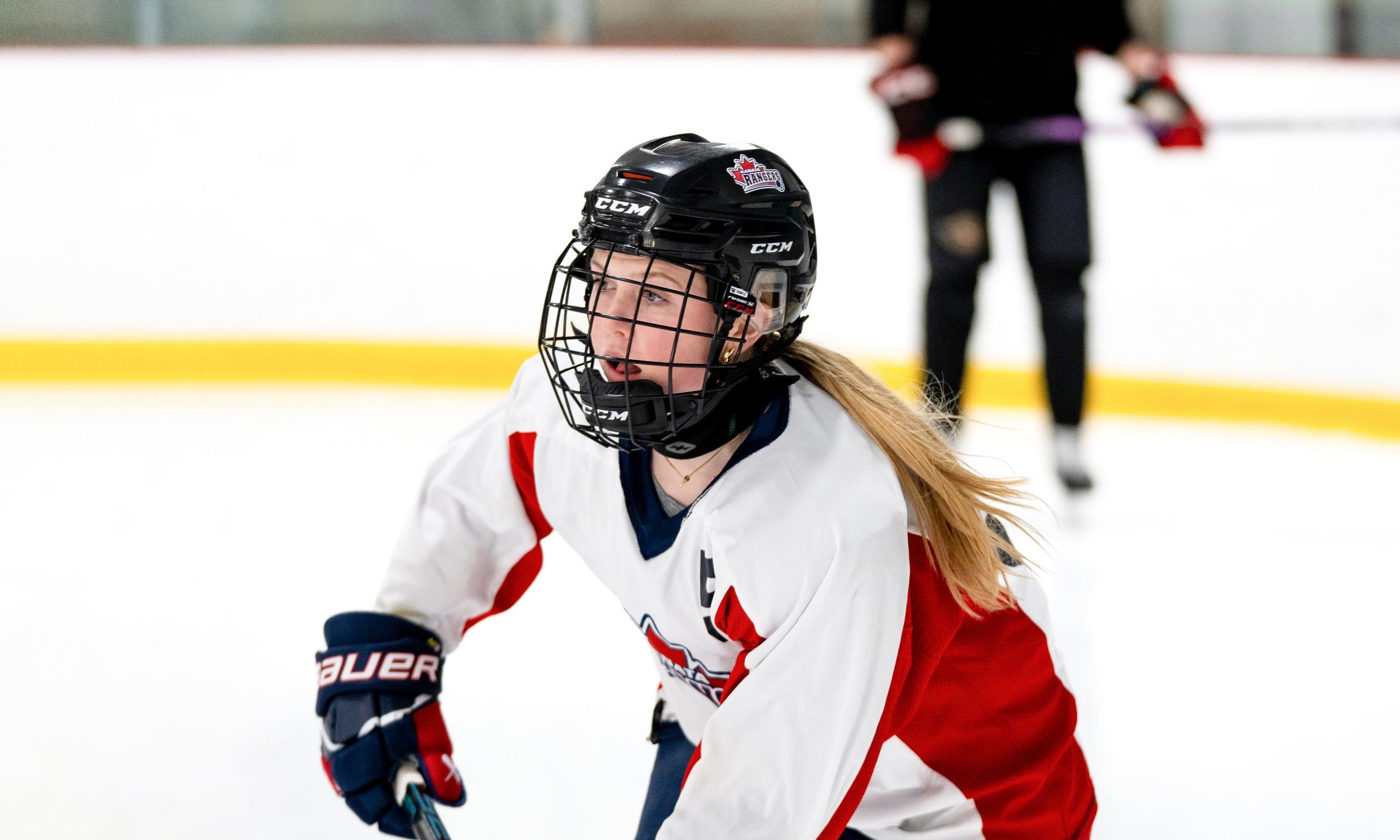 A female ice hockey player in action, wearing a white and red jersey, skates forward intently.