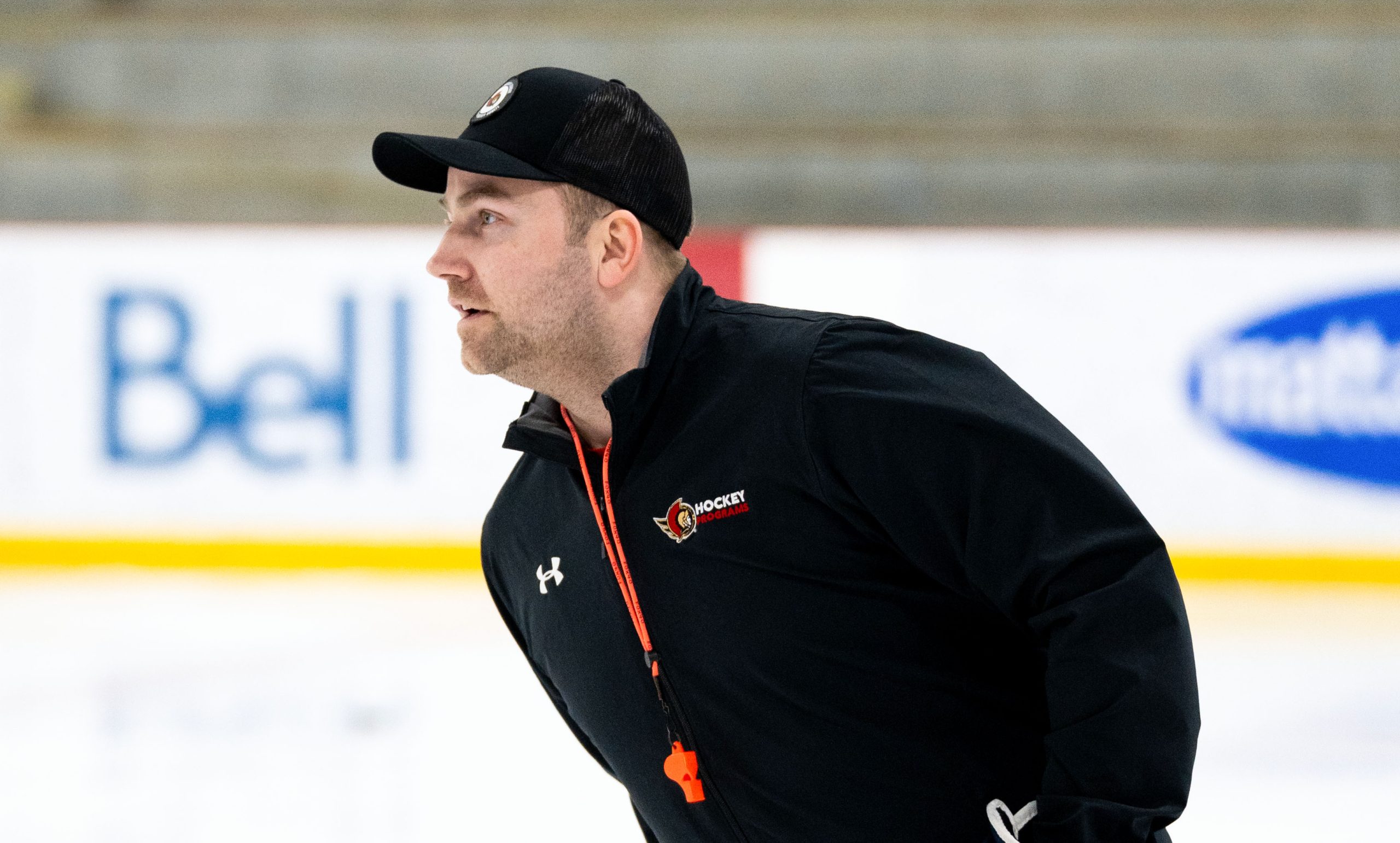 A hockey coach in black gear and a cap skates on the ice rink.